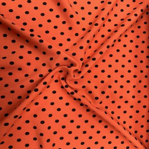 Crêpe polyester fond orange pois noirs